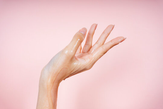 Woman hand coating with oily lotion on pink background.