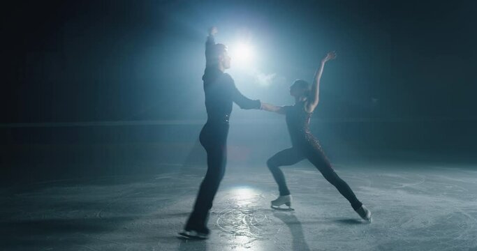 Cinematic shot of young couple of artistic figure skaters is performing a pair skating choreography on ice rink before start of a competition. Concept of perfection, precision, freedom, passion.