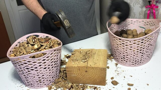A man pricks walnuts with a hammer. On a wooden block. Nuts are in the basket.