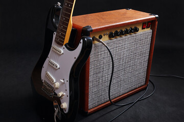 Combo amplifier for electric guitar with black guitar on black background.