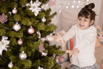 A funny dark-haired girl decorates a Christmas tree in the morning. In home clothes. Place for an inscription.