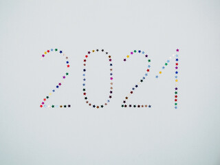 Isolated inscription 2021 from multicolored glittering stars confetti on a white background top view. New Year background with inscription 2021. Happy New Year 2021