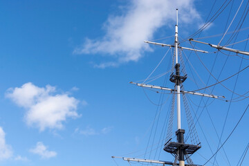 Old hip sailing mast against a blue sky with clouds background with copy space. Main old warship mast of a sailboat. Summer ocean vacation on a vessel frigate. Tie knots for ropes of water transport