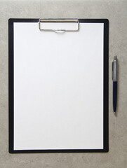 Template of white paper with a ballpoint pen on light grey concrete background in a black tablet with a clip. Concept of new idea, business plan and strategy, with empty space for text