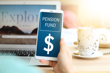 Woman holding mobile phone with open page of online pension fund on table