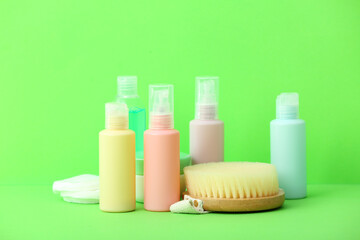 Dry body massage brush and set of travel bottles with body care cosmetics on color background