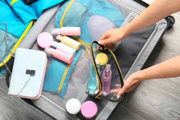 Female hands, bag with travel cosmetics kit and suitcase on floor