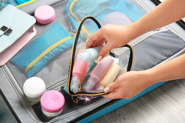 Female hands, bag with travel cosmetics kit and suitcase on floor