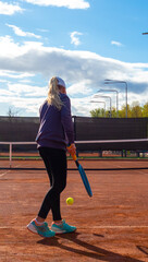 Cute blonde little girl with tennis racket and ball against blue sky in a summer. The concept of kids sport 