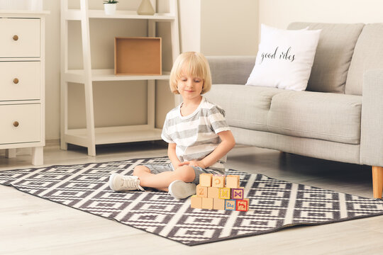 Cute little boy playing with wooden cubes on carpet at home