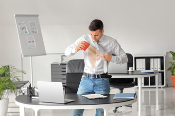 Stressed young businessman with coffee stains on his shirt and clipboard in office