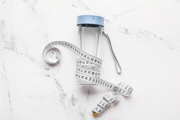 Bottle of water and measuring tape on light background