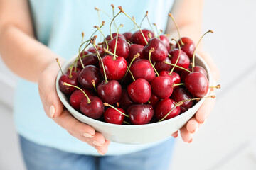 Woman with bowl of tasty cherry on light background