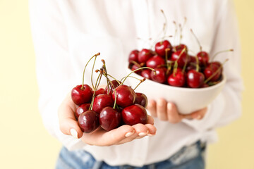 Woman with bowl of tasty cherry on color background