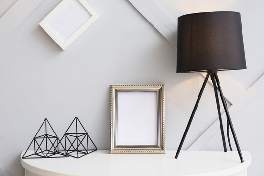 Blank photo frame and lamp on table in room