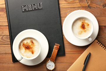 Cups of hot coffee and wristwatch on wooden table in cafe