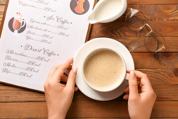 Female hands and cup of hot coffee on wooden table in cafe