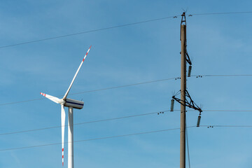 view of a modern windmill against a blue sky. The white blades of the wind turbine close up. Renewable energy source. old high voltage pole with wires next to modern wind turbine.