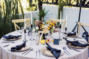 Round table decoration with flower center, high candles and black napkins and cutlery