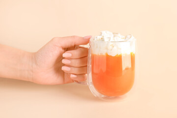 Female hand with cup of tasty pumpkin smoothie on color background