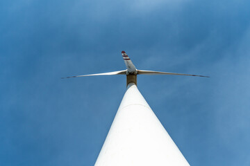 bottom view of a modern windmill against a blue sky. The white blades of the wind turbine. Clean...