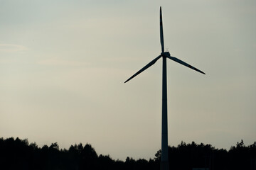 view of a modern windmill against a blue sky. The white blades of the wind turbine. Wind turbines in the forest away from the big city on a summer day. Clean and renewable energy production