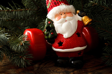 Small ceramic Santa Claus figurine and red dumbbell, with Christmas tree branches in background....