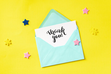 Thank You card in a teal blue envelope, shot from above on a yellow background with stars and glitters