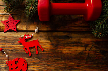 Red dumbbell, Christmas tree branches and decorative ornaments. Healthy fitness lifestyle holiday season concept. Flat lay composition with copyspace on wooden background.