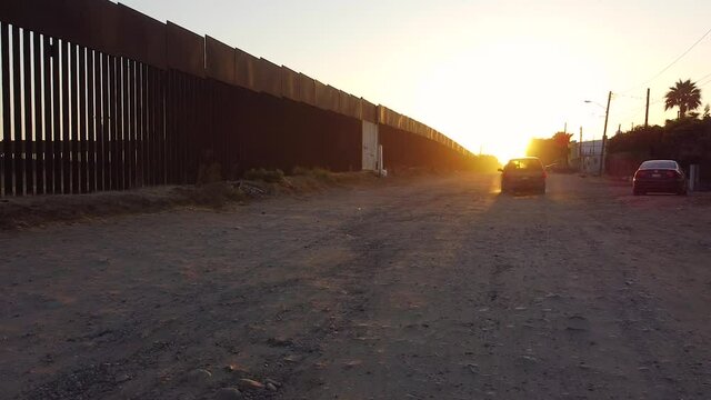 A large car speeds up and drives into toward the rising sun along the ever contentious U.S.-Mexico border on the Mexican side, kicking up a proverbial cloud of dust which lingers in the golden light.