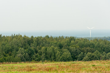 view of a modern windmill against a blue sky. The white blades of the wind turbine. Wind turbines in the forest away from the big city on a summer day. Clean and renewable energy production