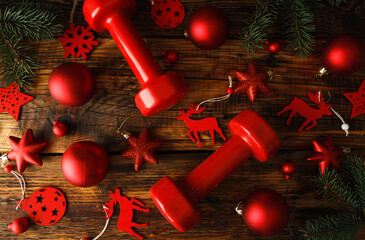 Two red dumbbells, Christmas tree branches with decorations, ornaments and baubles. Healthy fitness lifestyle holiday season concept. Flat lay composition on wooden background.