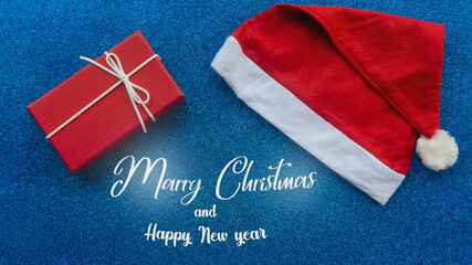 Santa Claus hat and New Years gift on blue glittering New Years background. Merry Christmas lettering. New Year concept
