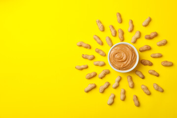 Sun made of peanut and bowl of peanut butter on yellow background