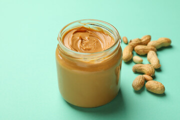 Jar with peanut butter and peanut on mint background