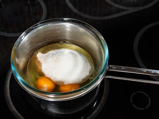 cooking sweet sponge cake at home - above view of sugar with cinnamon on raw eggs in glass bowl on water bath on stove at home kitchen