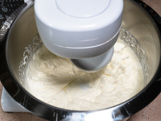 cooking sweet sponge cake at home - above view of whipping of liquid cream with sugar in steel bowl of food processor at home kitchen (mixer whisk blurred in motion)