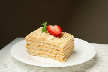 Plate with piece of Napoleon cake on white wooden background, close up