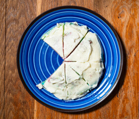cooking sweet sponge cake at home - top view of cutted homemade sponge cake covered by whipped cream on blue plate on wooden table at home kitchen