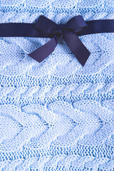 Beautiful wool knitted background in the pale blue color made like a present with the dark blue ribbon.