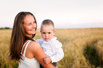 Fototapeta premium Caucasian beautiful mother hugs her child son in the summer wheat field at sunset, summer and harvest, natural products and relaxation in the countryside, motherhood