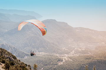 A paraglider with an instructor and a student soars against the background of wooded mountains and...