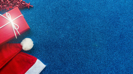 Christmas background. Santa Claus hat, gift, toy tree on blue glitter background. View from above