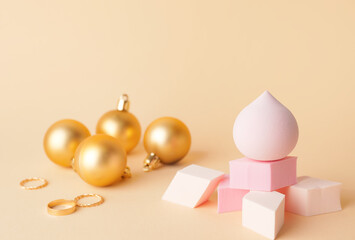 Christmas balls and makeup sponges on color background