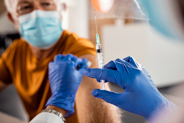 Close-up of doctor vaccinating senior man due to COVID-19 pandemic.
