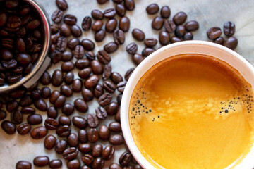 Top view of a cup of American coffee with a nice crema on the top on a concrete table with a pile of organic arabica coffee beans and filter holder basket nearby.