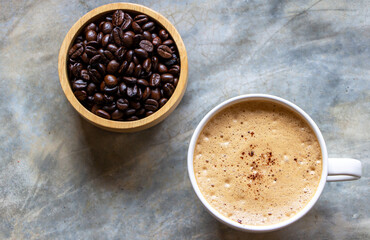  cup of mocha coffee with a nice foam on top on a concrete table and a wooden bowl of organic arabica coffee beans nearby.