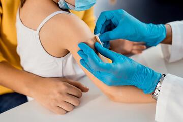 Close-up of doctor placing adhesive bandage on little girl's arm after vaccination.