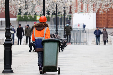 Worker carries a garbage can down the street. Cleaning the city streets during covid-19 coronavirus pandemic