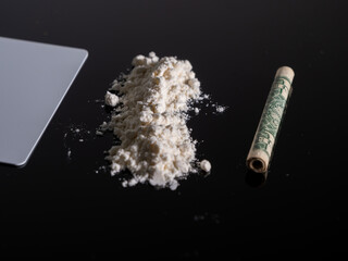 Lines of cocaine and a dollar bill. Cocaine lines shots on a black table glass. Cocaine powder, Credit card, close up, toned. Drug abuse concept. White poder on black table